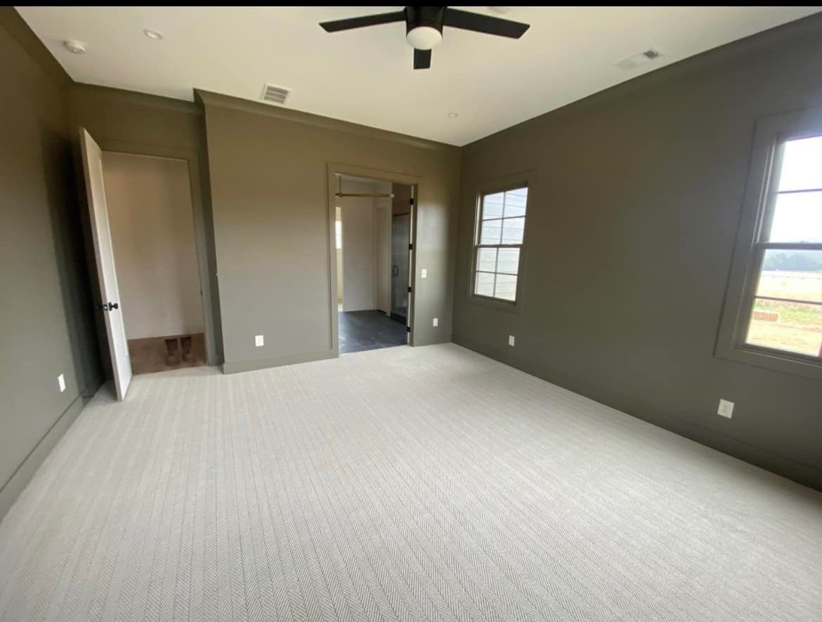 An empty bedroom with a ceiling fan and two windows.