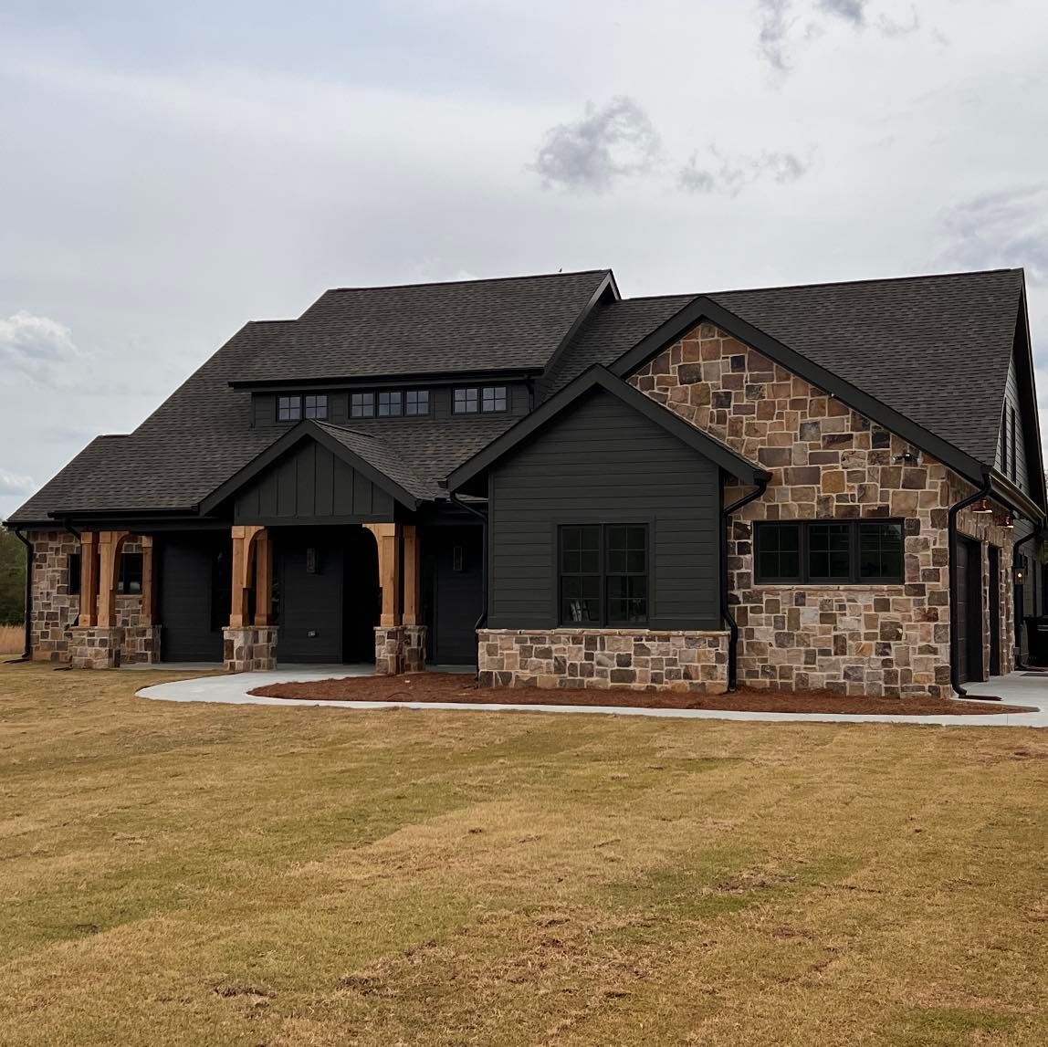 A large house with a black roof and a stone facade is sitting on top of a lush green field.