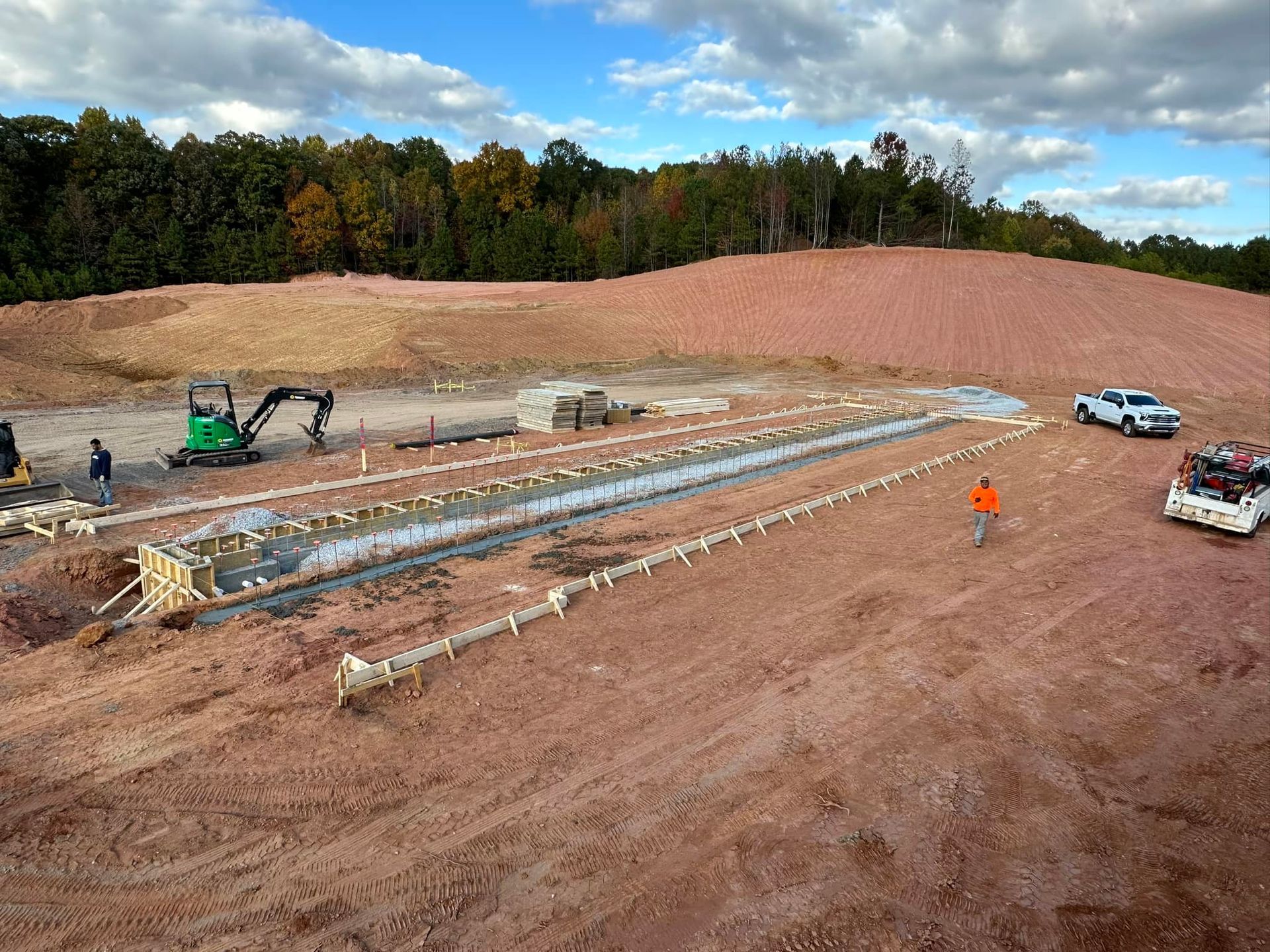 An aerial view of a construction site with a green excavator and trucks.