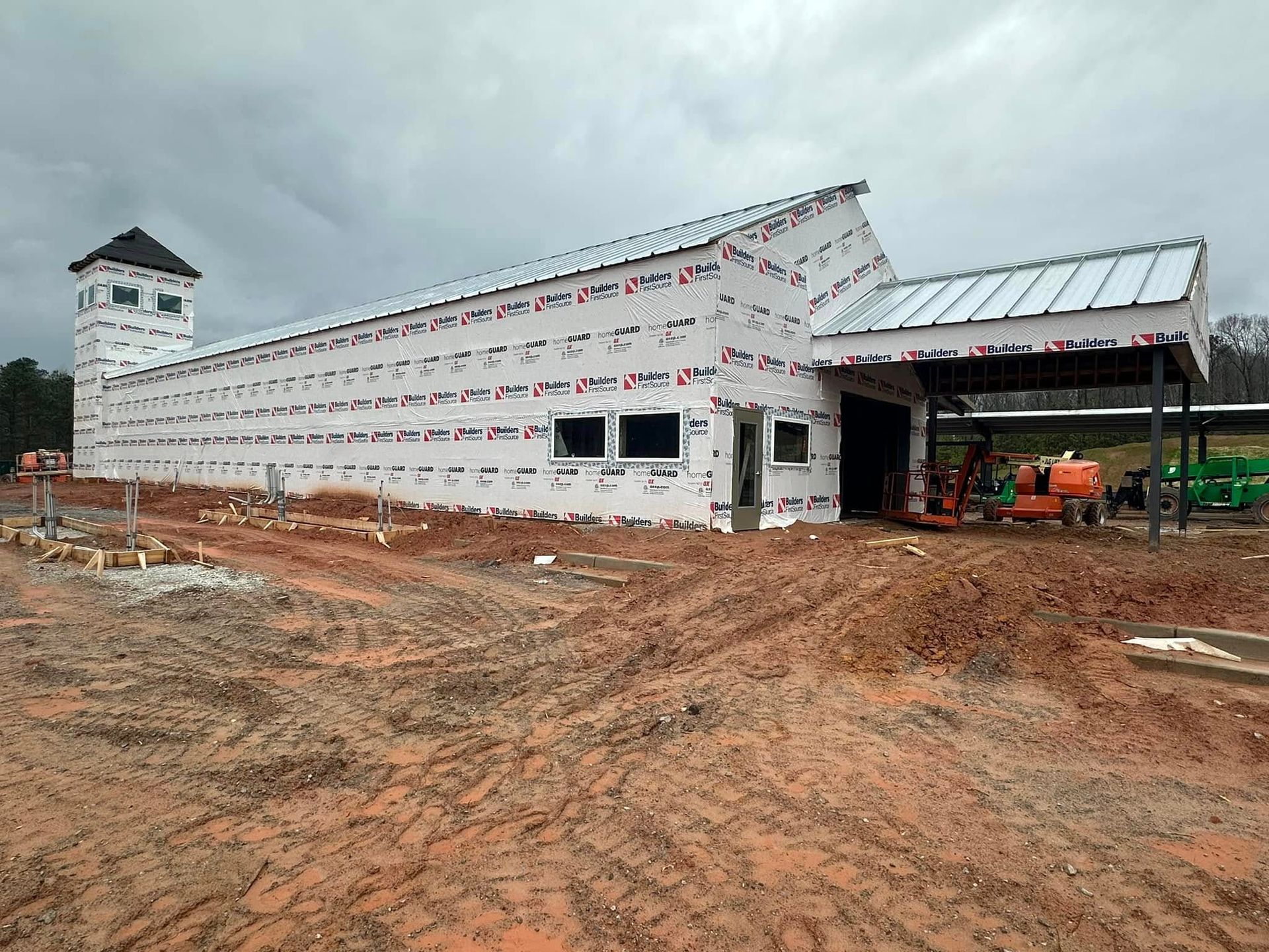 A large white building is being built in a dirt field.