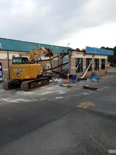 A yellow excavator is demolishing a building on the side of the road.