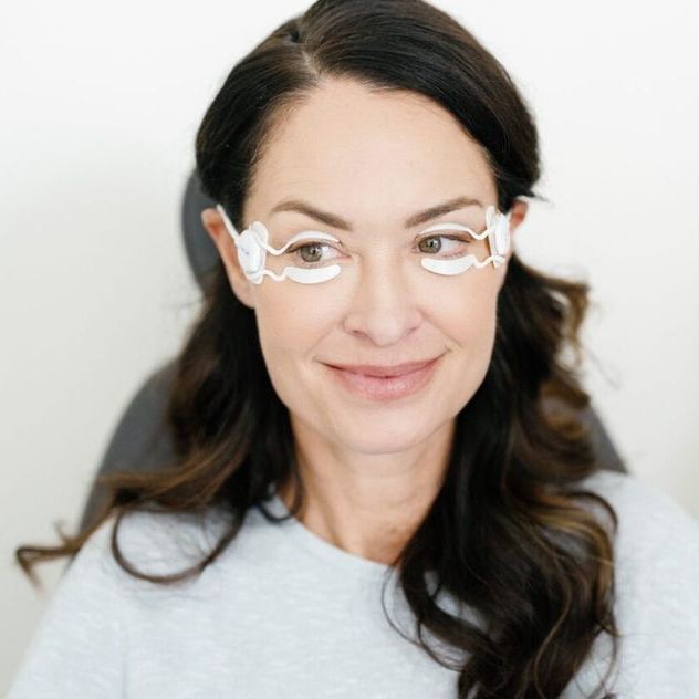 Woman wearing white eye-mask device; smiling, medium shot.