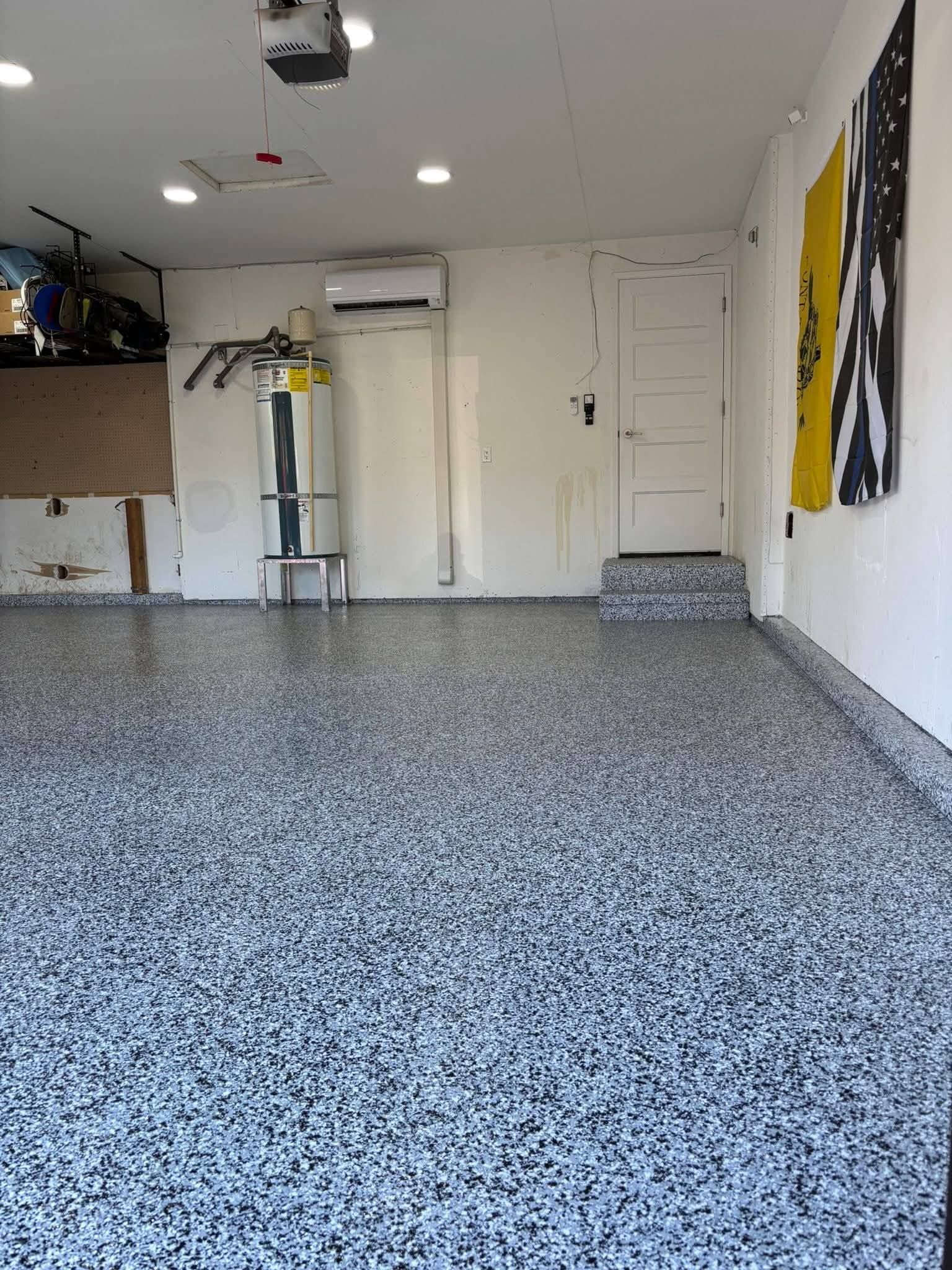 Empty garage with speckled gray floor, white walls, and a wall-mounted air conditioner.