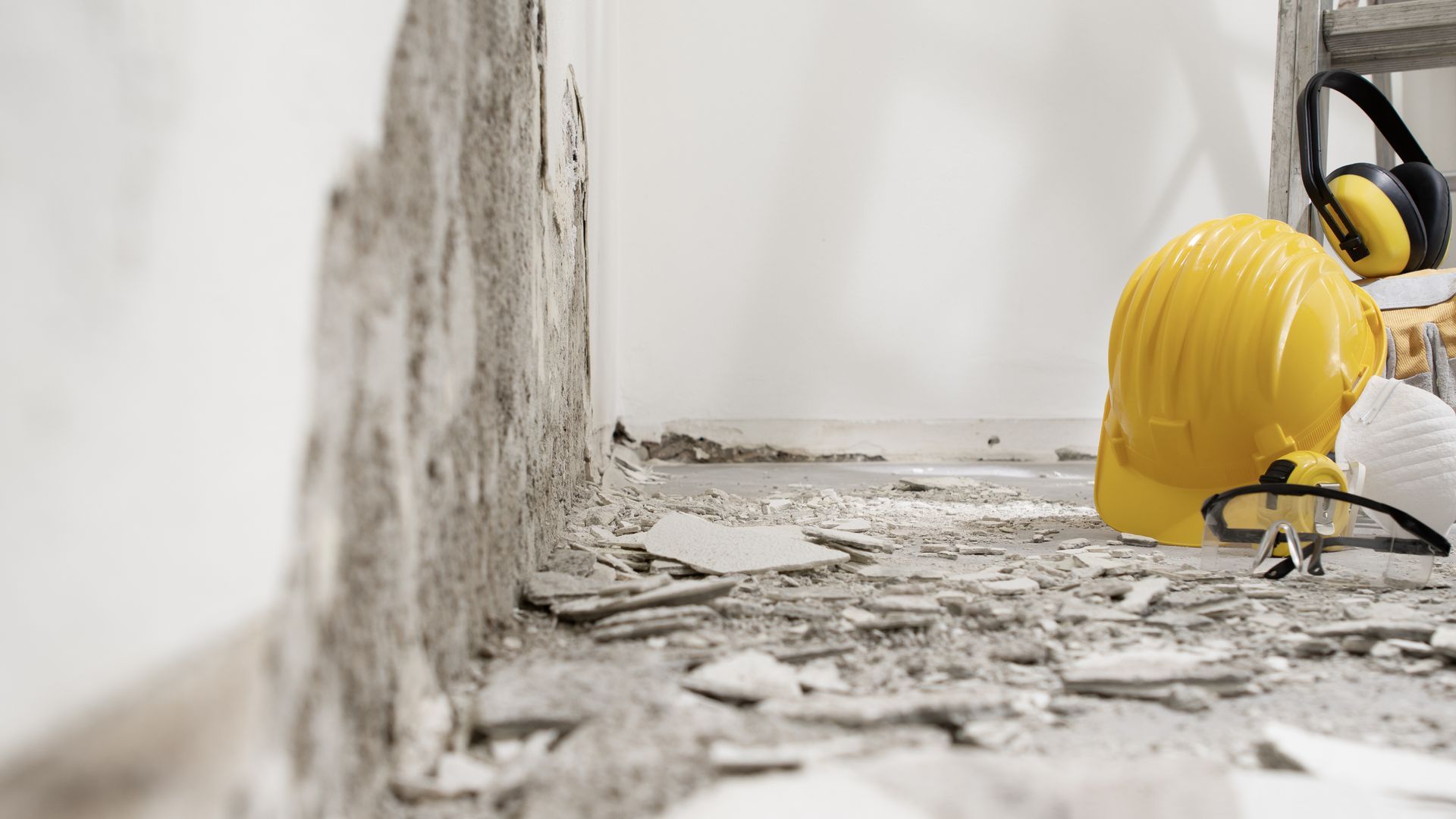 Construction worker in yellow hard hat inspecting damaged wall and rubble inside a room