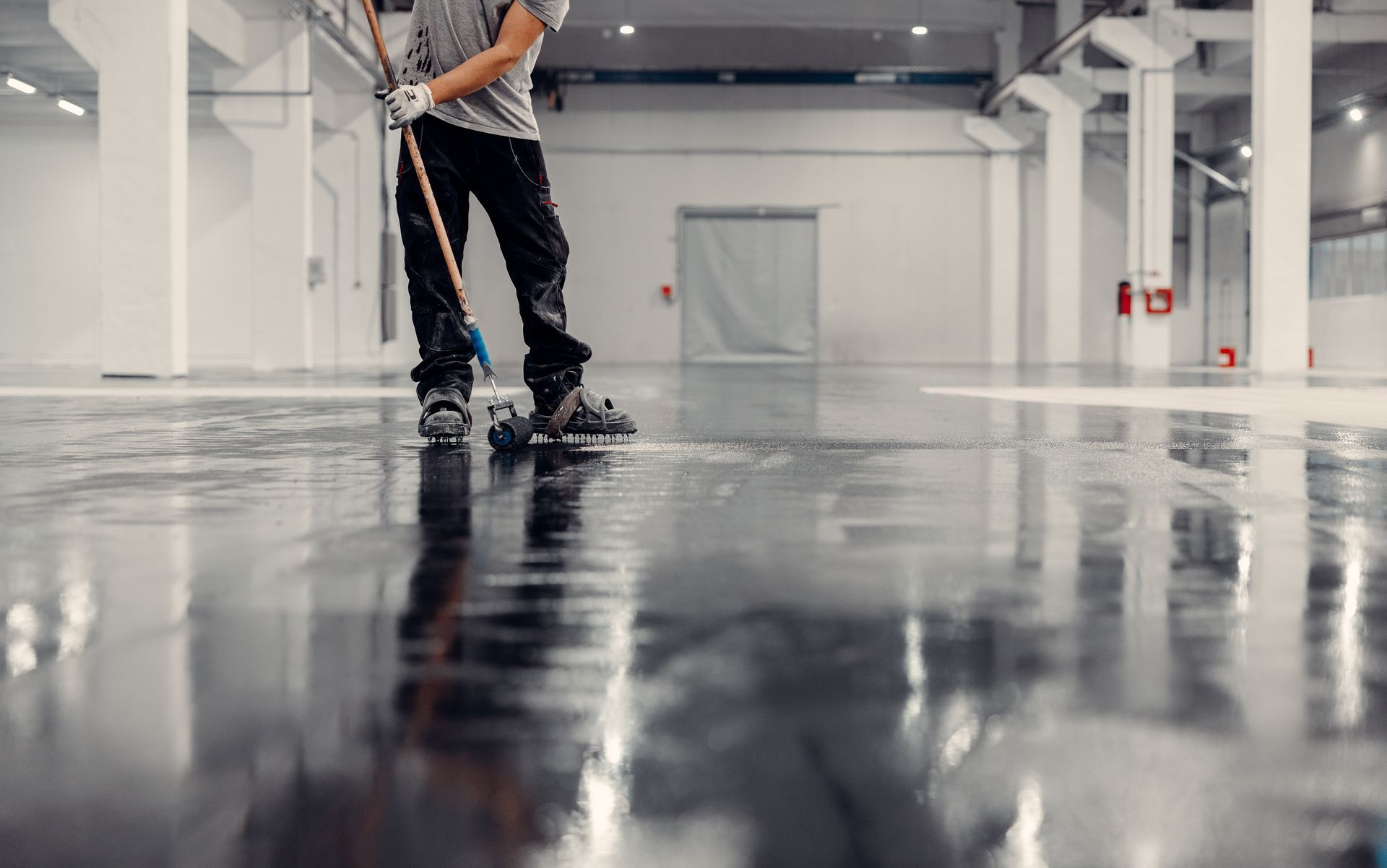 Worker mopping a glossy floor in a bright, empty warehouse