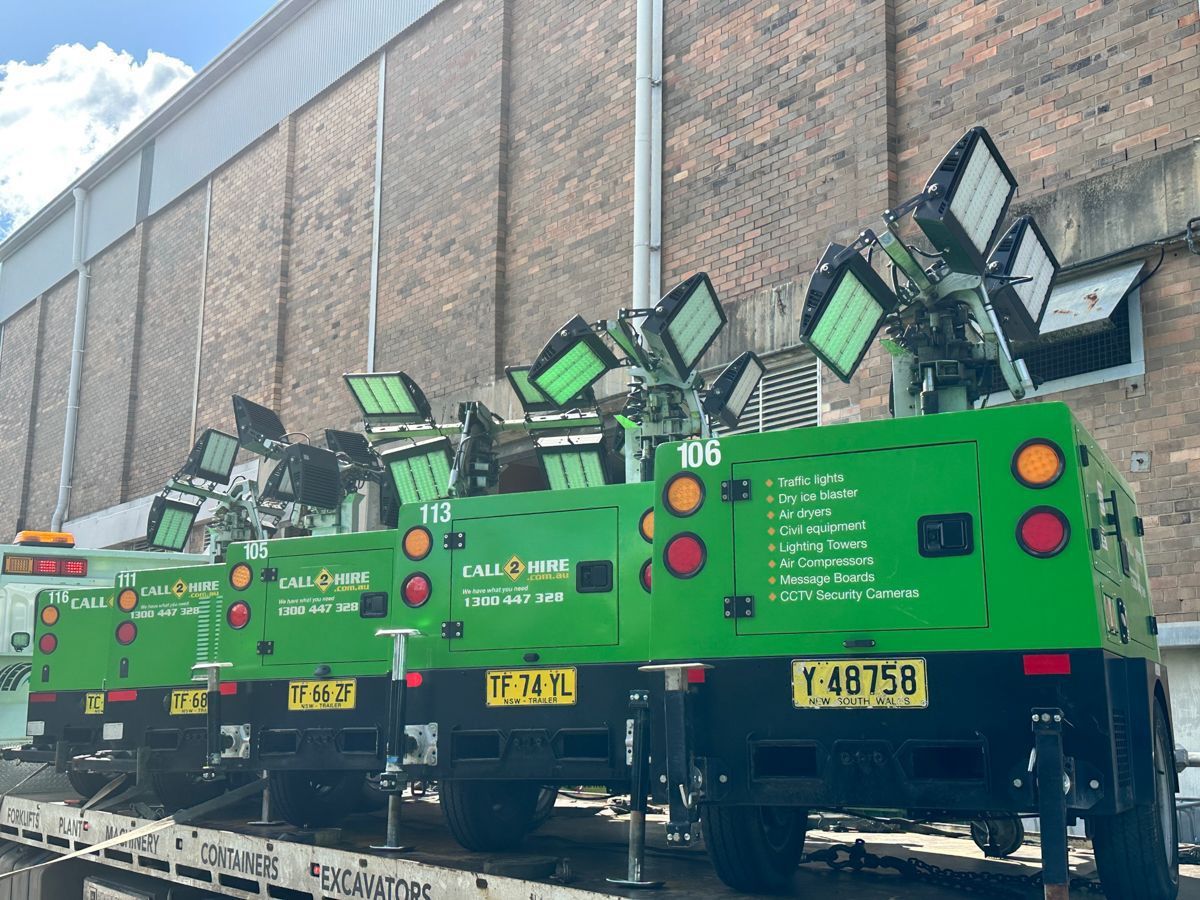 A row of bright green portable light towers parked on a trailer in front of a brick building.