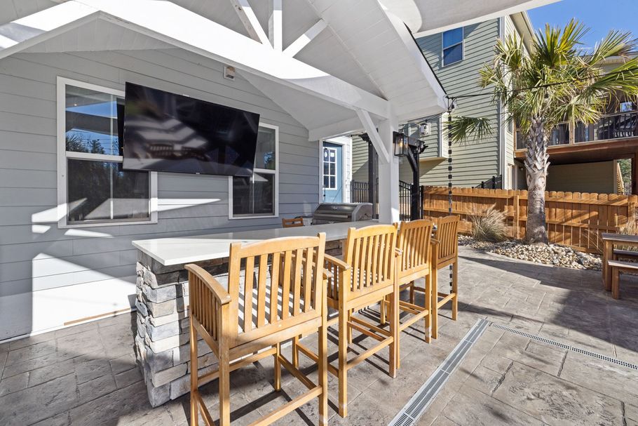 Outdoor patio with wooden chairs, stone table, and white pergola beside a house.