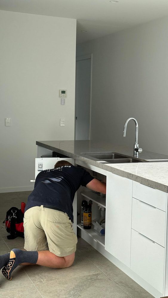A Man is Kneeling Down in a Kitchen Looking Under a Sink — R.K. Plumbing & Gas In Bli Bli, QLD