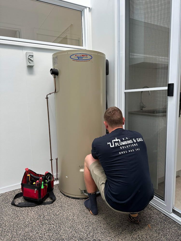A Man is Kneeling Down Next to a Water Heater — R.K. Plumbing & Gas In Bli Bli, QLD