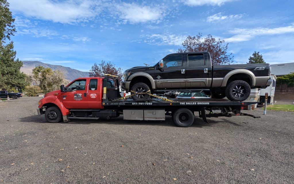 A tow truck is carrying a black truck and a red truck.