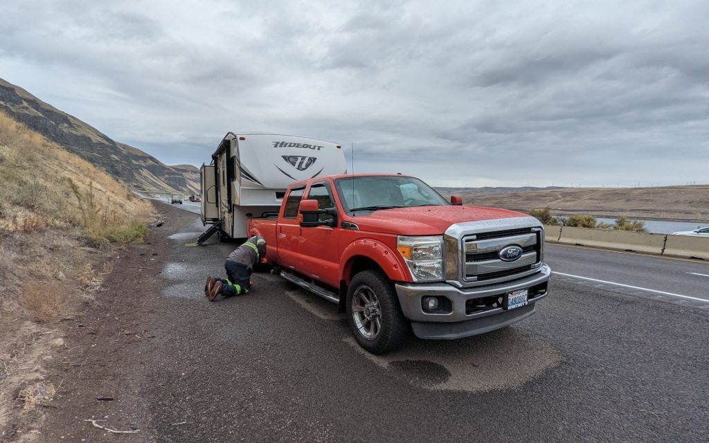 A man is kneeling next to a red truck with a trailer attached to it.