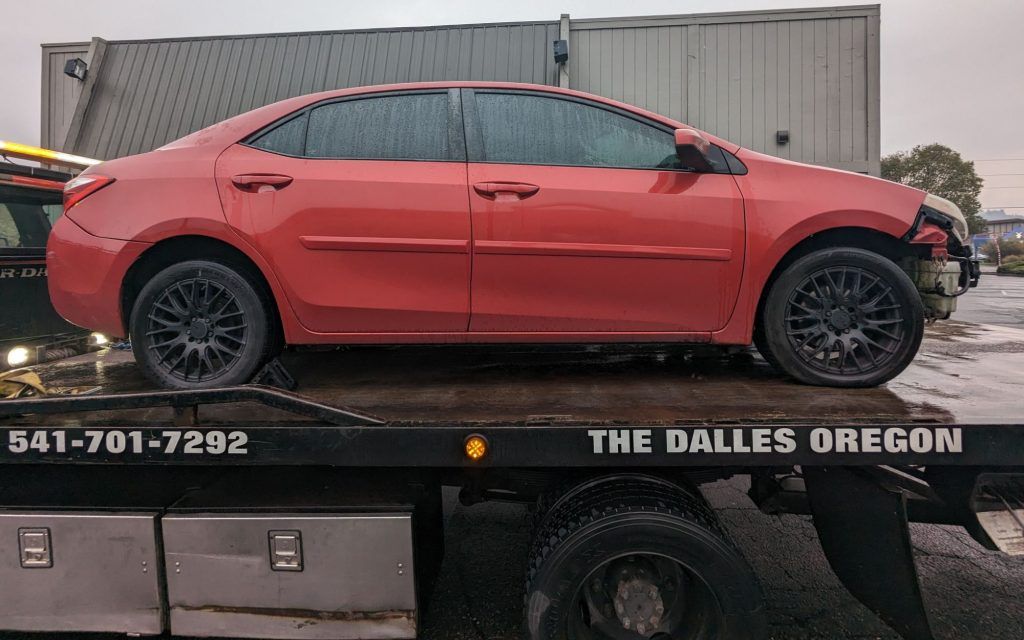 A red car is sitting on top of a tow truck.