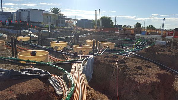 A construction site with a lot of pipes and buckets in the dirt.