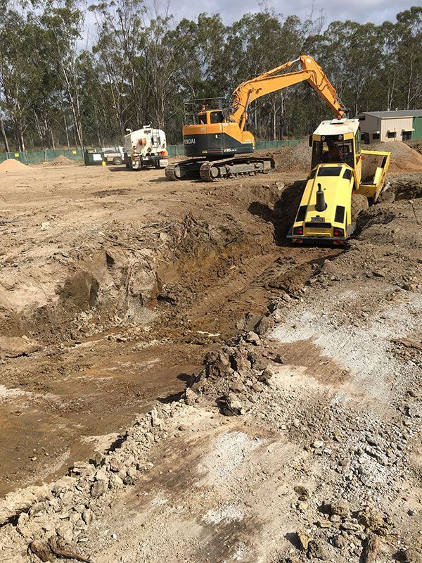A yellow excavator is digging a hole in a dirt field.