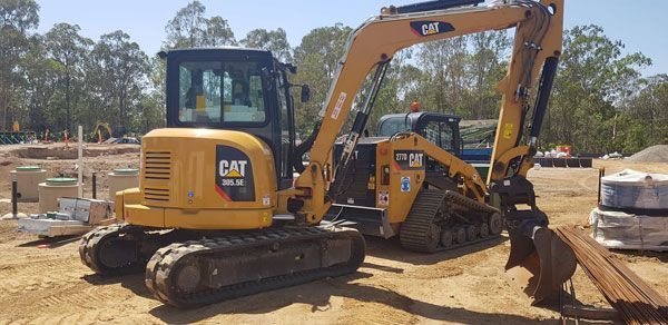 A couple of excavators are parked next to each other in a dirt field.