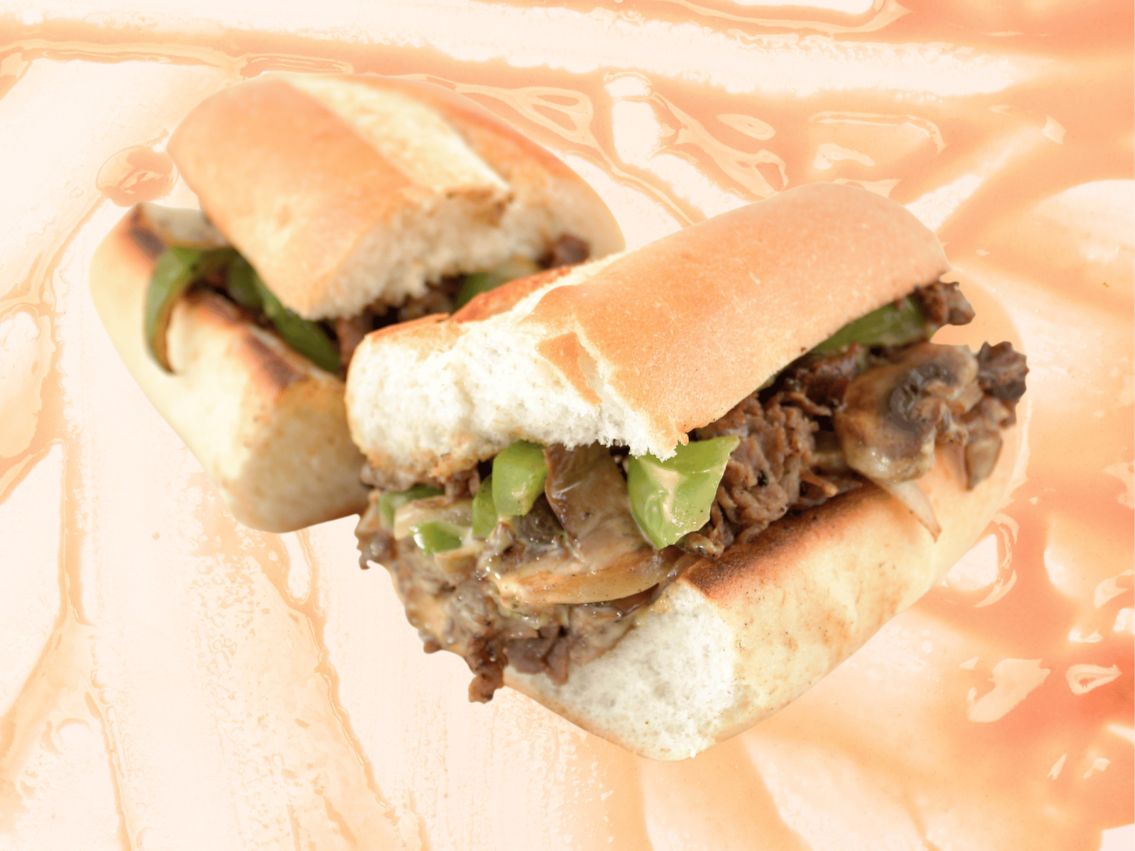 Two sub sandwiches with meat and green peppers on a bun