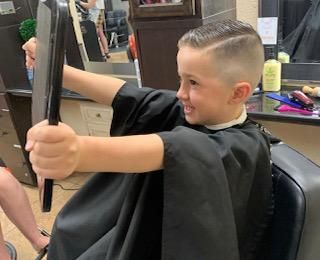 A young boy is sitting in a barber chair holding a mirror.