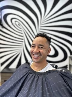 A man is smiling while getting his hair cut in a barber shop.