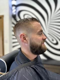 A man with a beard is getting his hair cut at a barber shop.
