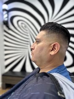 A man is getting his hair cut at a barber shop in front of a striped wall.