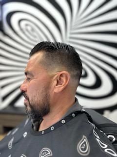 A man is getting his hair cut at a barber shop in front of a striped wall.