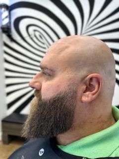 A bald man with a beard is getting his hair cut at a barber shop.