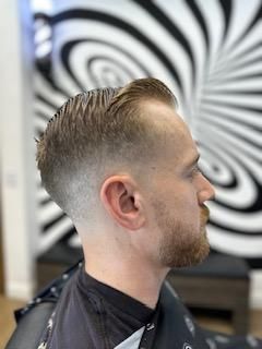 A man with a beard is getting his hair cut at a barber shop.