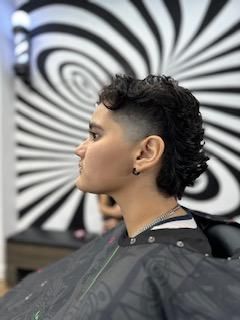 A woman is getting her hair cut in a barber shop in front of a striped wall.