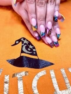 A close up of a woman 's nails on an orange shirt with a witch hat on it
