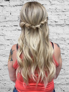 A woman with long blonde hair is wearing a half up half down hairstyle.