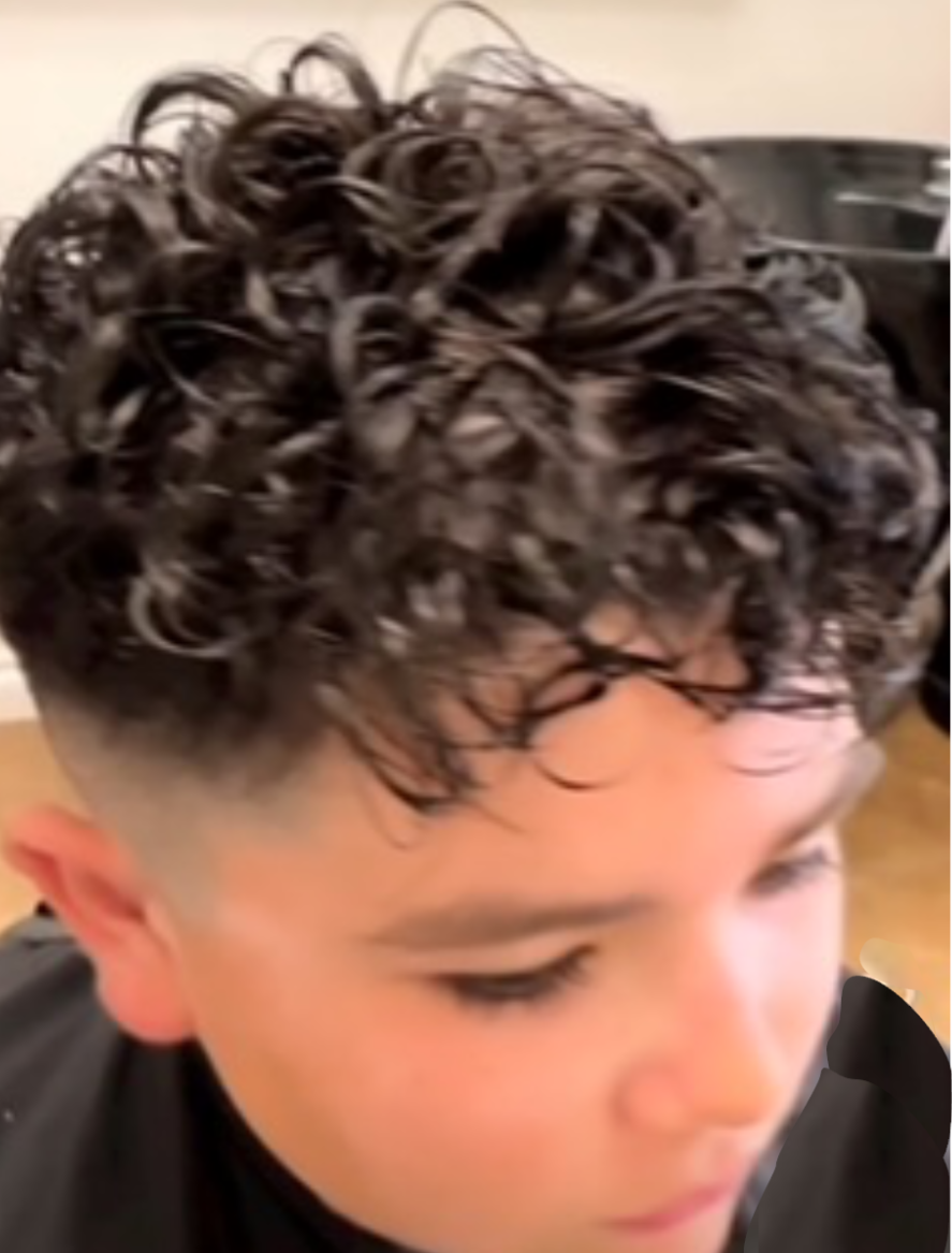 A young boy with curly hair is getting his hair cut.
