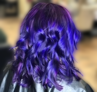 A woman with purple hair is wearing a black cape