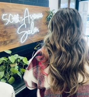A woman is standing in front of a 50th avenue salon sign.