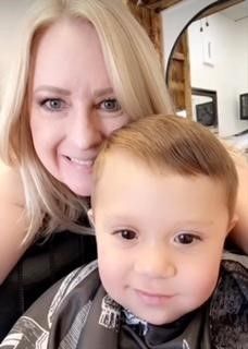 A woman is sitting next to a little boy in a barber shop.