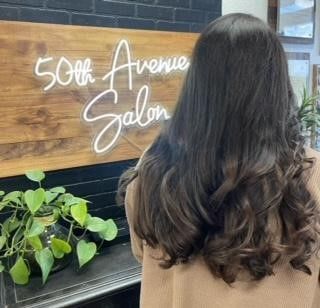 A woman is standing in front of a sign that says 50th avenue salon.
