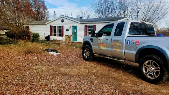 Silver pickup truck parked in front of a white house with red shutters and a teal door on a fall day.