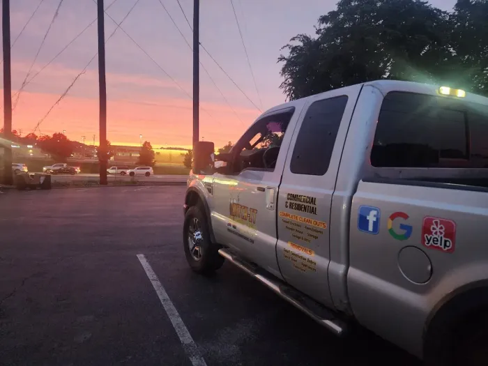 Silver pickup truck parked at dusk with a colorful sunset in the background. Social media icons are visible on the truck.