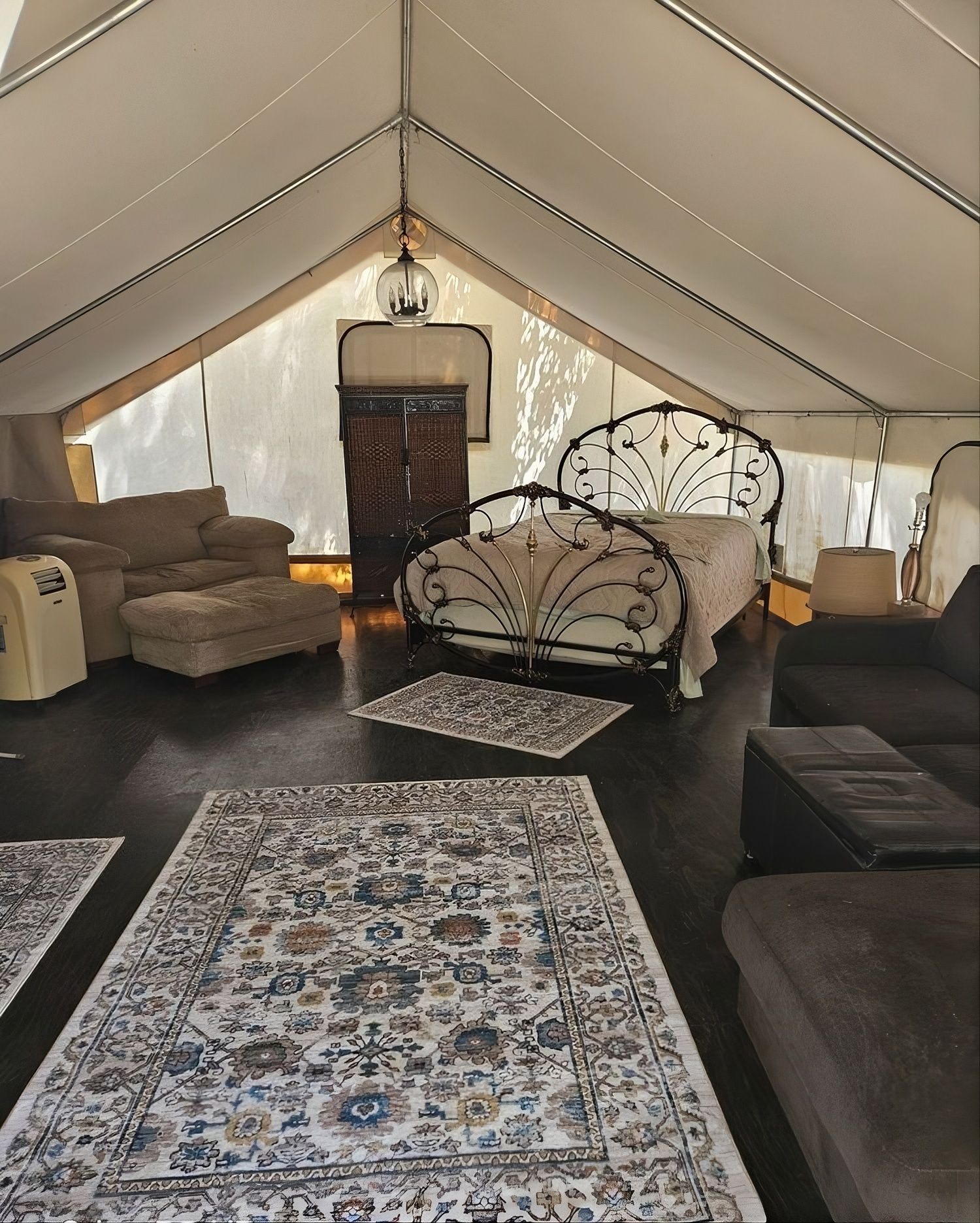 Inside of a glamping tent with bed, rugs, sofa, and a decorative cabinet.