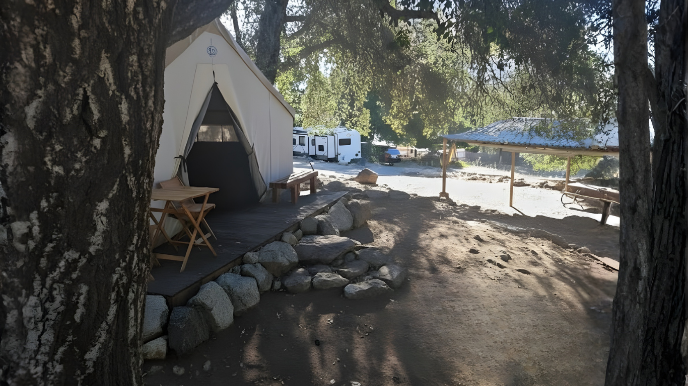 RVs parked under a metal awning on a cloudy day. Two people sit outside one RV.