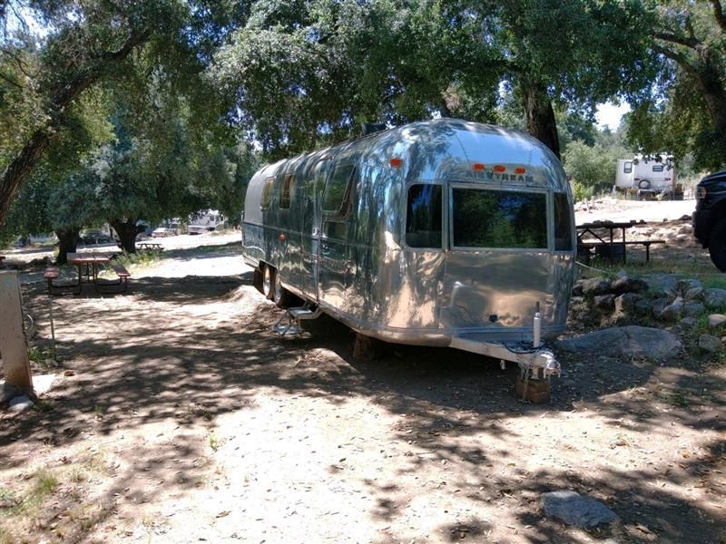 Shiny silver Airstream trailer parked under trees in a campground.