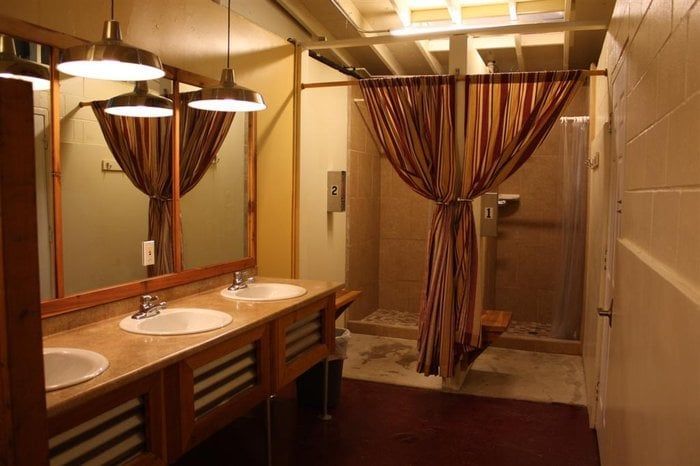 Bathroom with sinks, mirrors, and a shower stall with a curtain. Pendant lights and wood accents present.