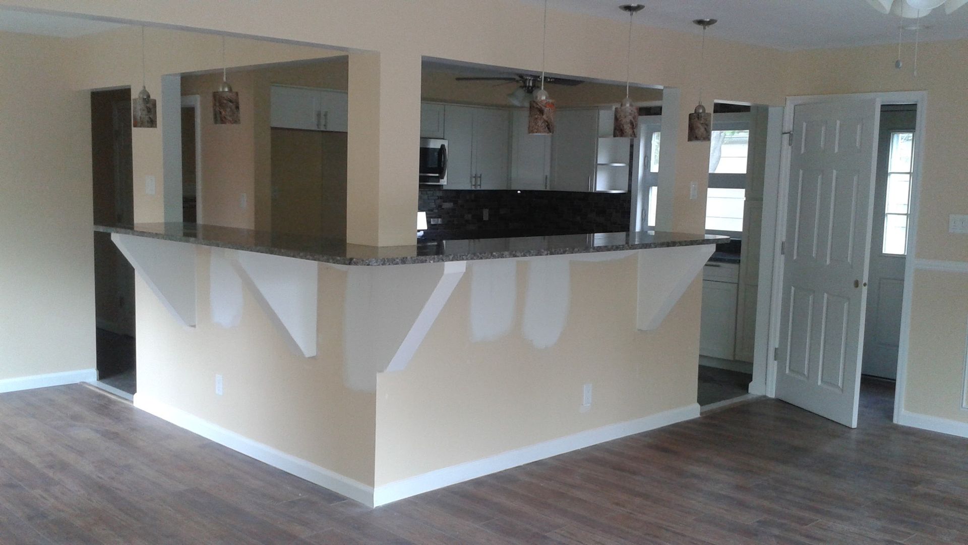 An interior view of a kitchen with a granite peninsula, unpainted drywall patches, and wood-look flooring.