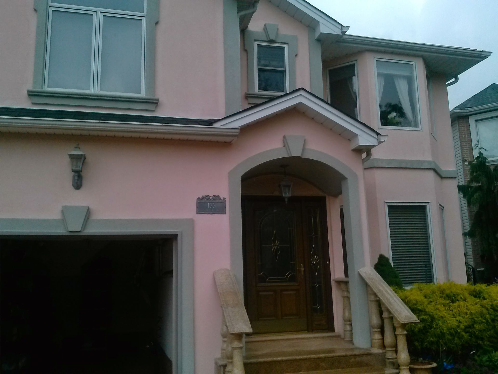 A two-story house painted light pink with grey trim, a garage, and a covered front entryway with a wooden door.
