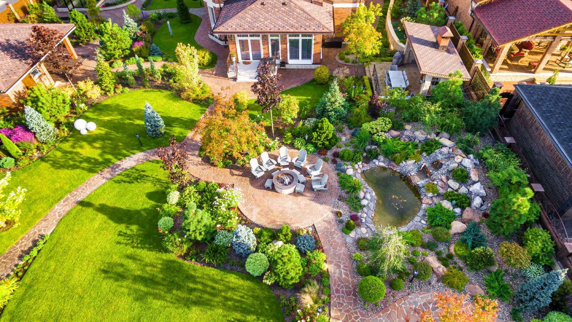 Aerial view of a beautifully landscaped backyard with a house, lawn, garden, winding stone path, and a pond.