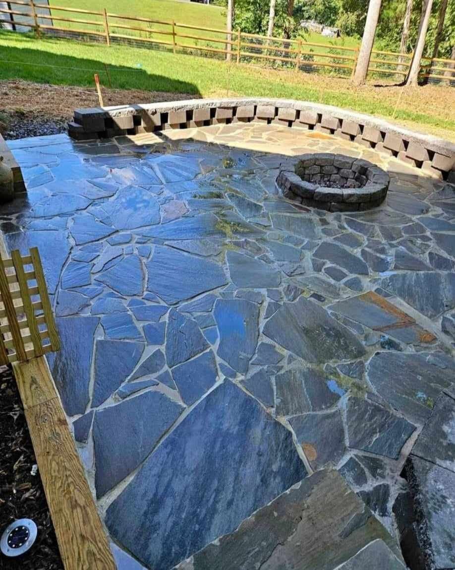 Stone patio with a fire pit, surrounded by a retaining wall and wooden fence, with a blueish-gray color.