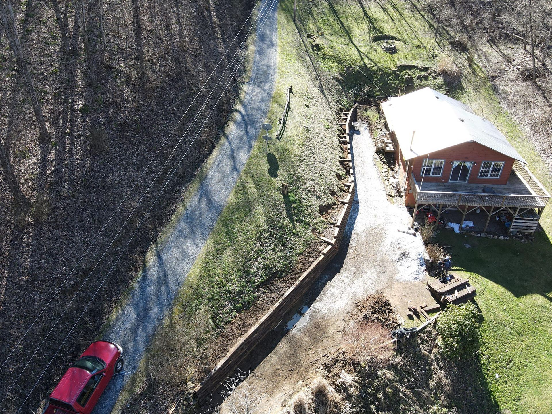 Overhead view of a red truck on a paved road beside a long retaining wall and a house with a deck.
