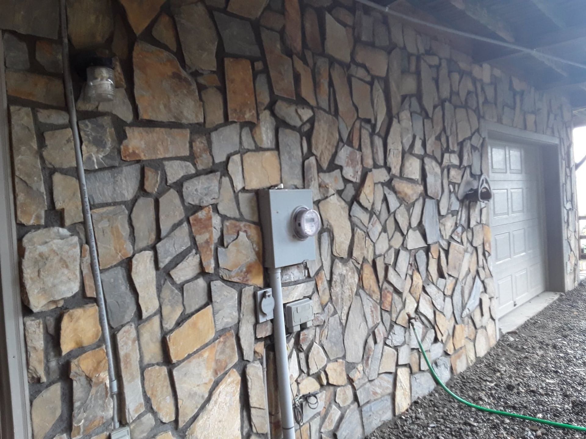 Stone exterior wall with electrical meter and outlets; a white garage door is visible.