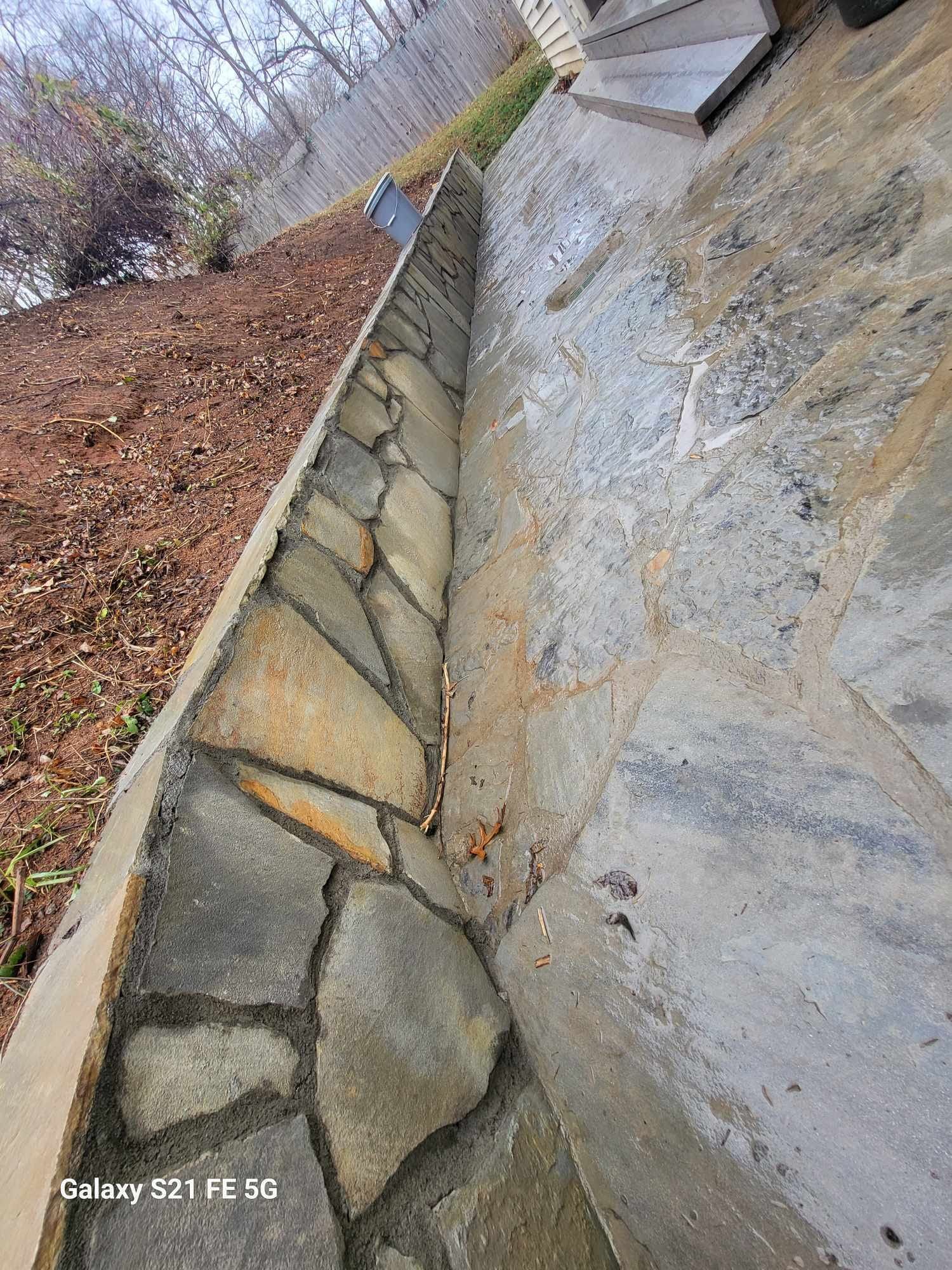 Stone retaining wall and steps in an outdoor setting, with a narrow channel of stone and mortar between them.