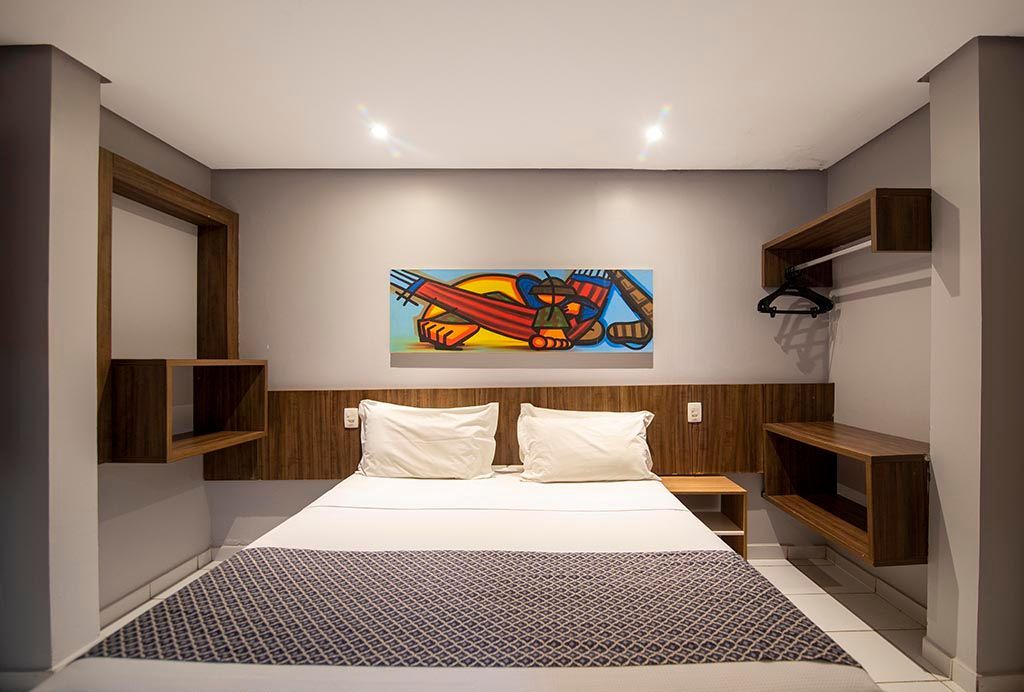 Um quarto com uma cama grande e uma pintura na parede. Netuanah Praia Hotel