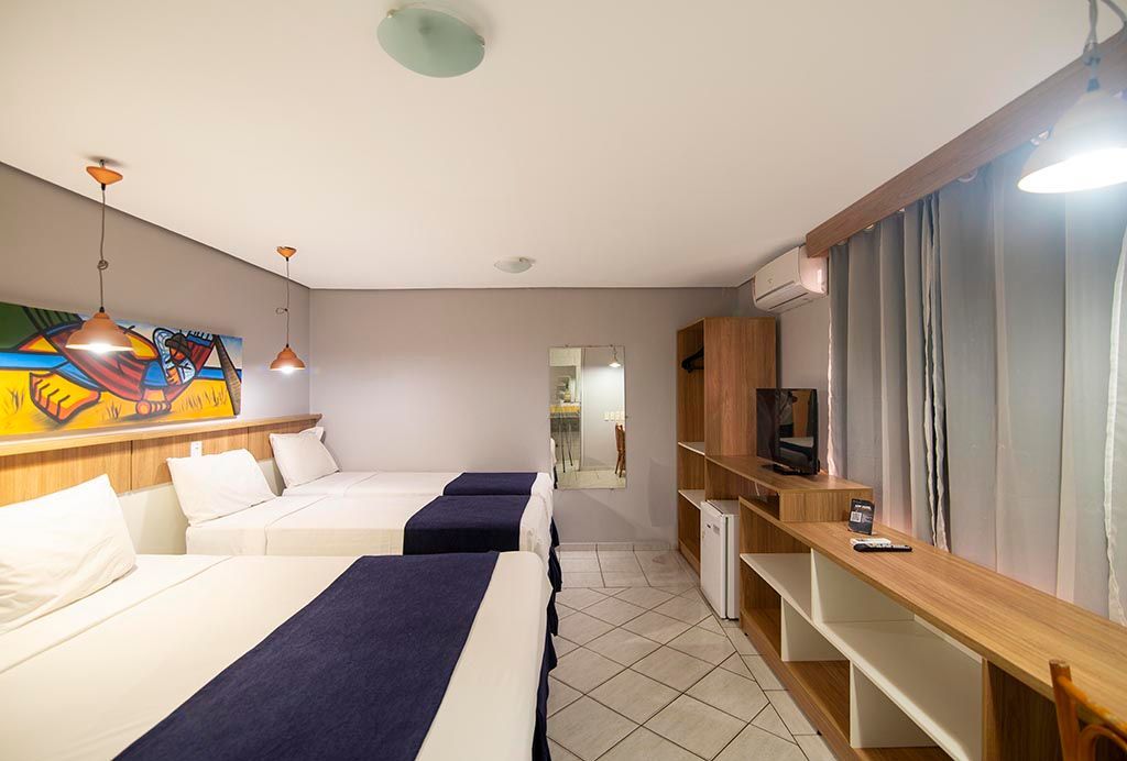 Um quarto de hotel com três camas e uma televisão. Netuanah Praia Hotel